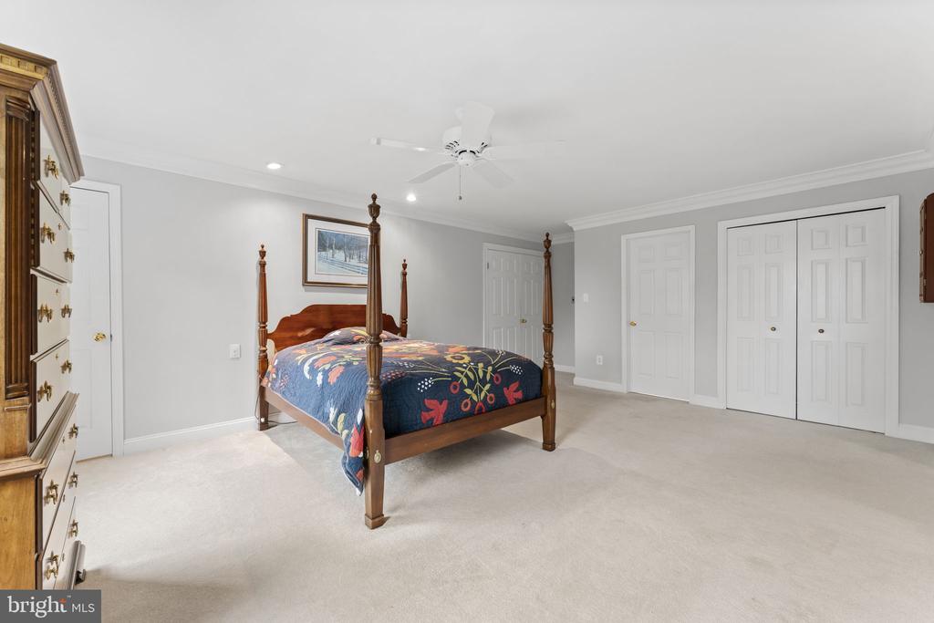 Bedroom with a dark wood four-poster bed and colorful floral quilt, white closets along the far wall.