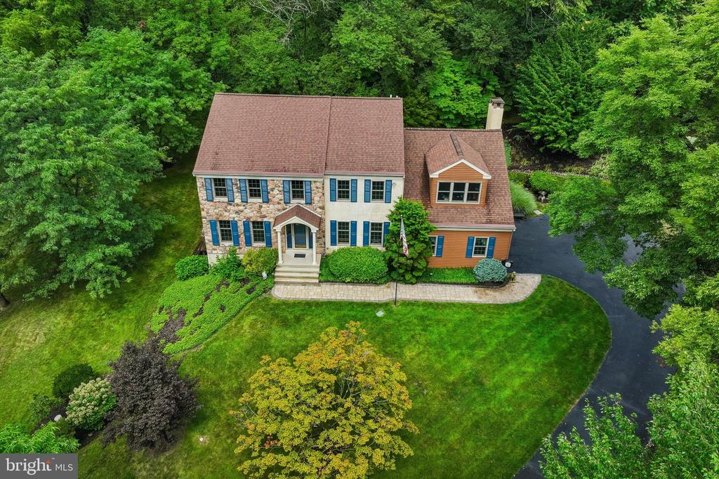Aerial view of a stone-and-siding home surrounded by mature trees, with a curved driveway and landscaped lawn.