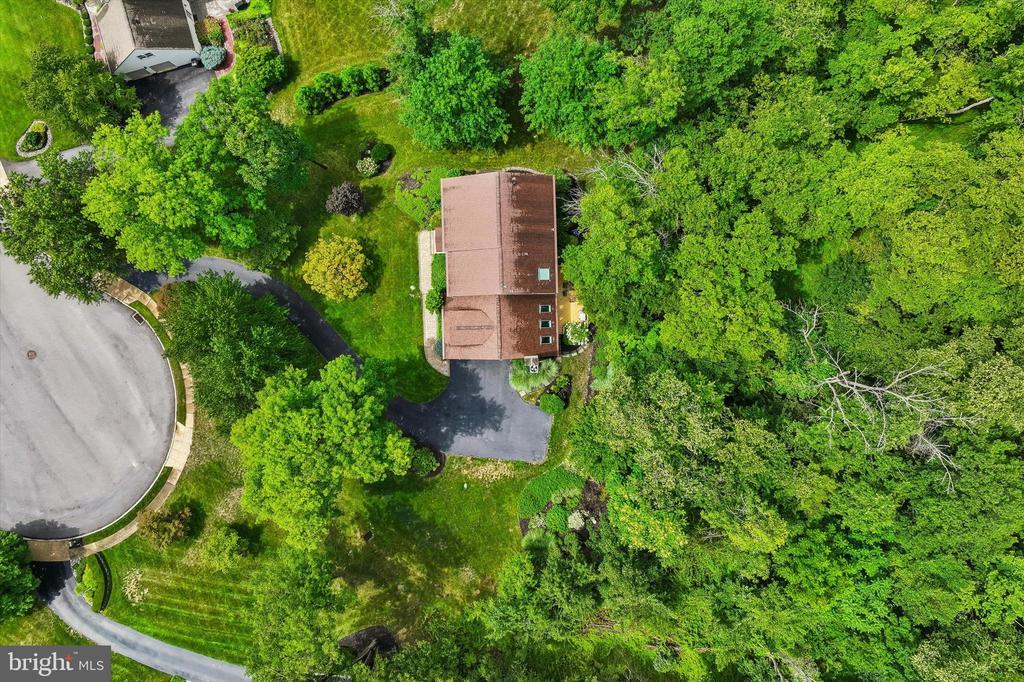 Aerial view of a home surrounded by dense trees, with a driveway and cul-de-sac.