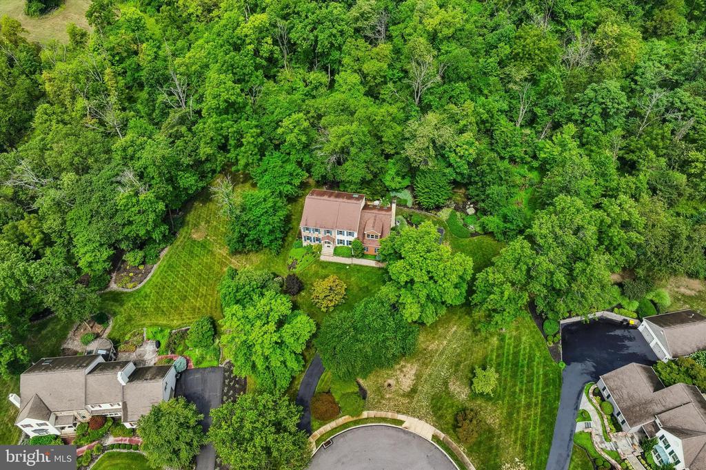 Aerial view of a home surrounded by mature trees and lawn near a cul-de-sac.