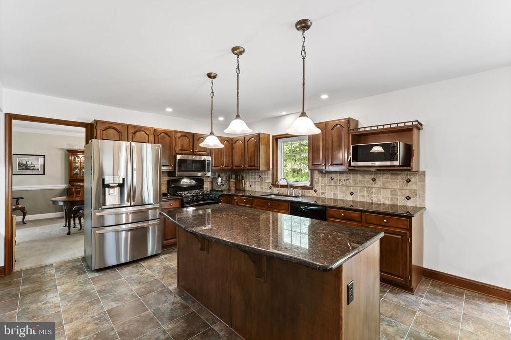 Kitchen with a large granite island, dark wood cabinetry, and stainless steel appliances.