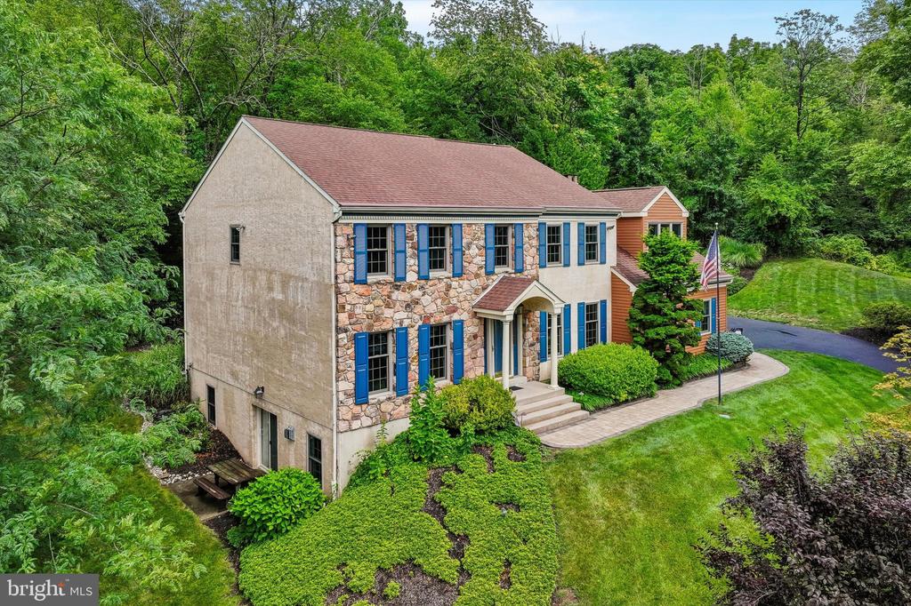 Two-story stone-and-stucco house with blue shutters, landscaped grounds, and wooded surroundings.