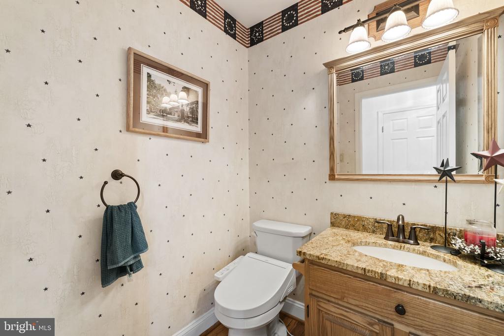 Bathroom with a wood vanity, granite countertop, large mirror, and star-patterned wallpaper.