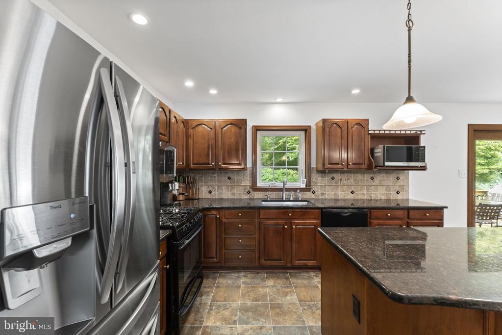 Kitchen with dark wood cabinets, granite island, stainless steel appliances, and a garden view.