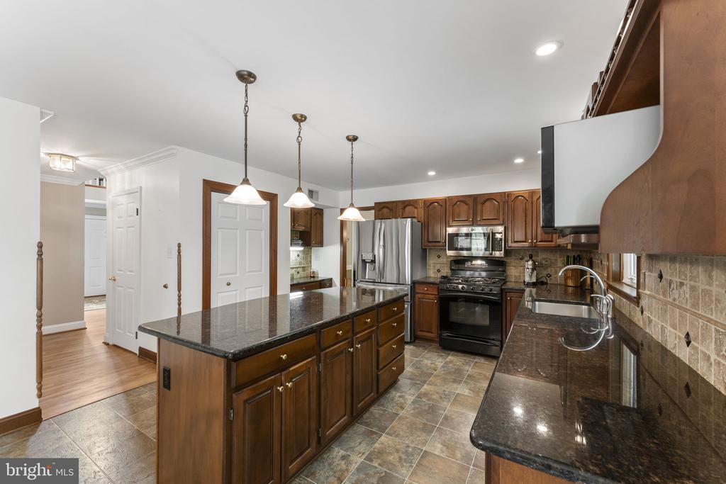 Kitchen with dark wood cabinets, granite counters, stainless steel appliances, and a large central island.