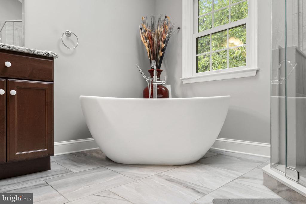 Bathroom with a freestanding tub, gray tile, glass shower, and dark wood vanity.