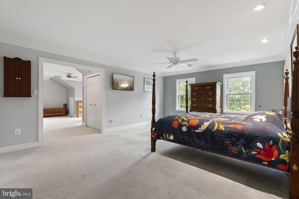 Bedroom with a dark four-poster bed, colorful floral quilt, and two sunlit windows.