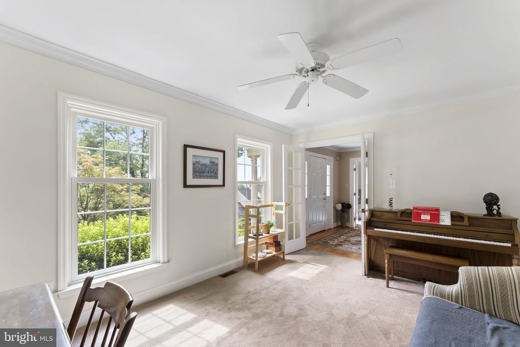 Carpeted living room with a wooden upright piano, large windows, and French doors.