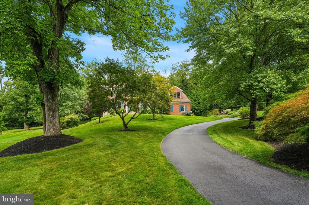 Brick house beyond a curving driveway, surrounded by mature trees and a broad green lawn.