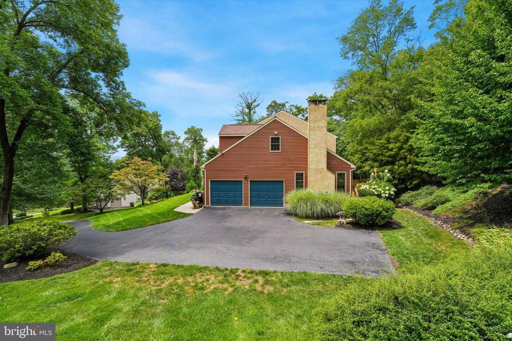 Red-sided house with two blue garage doors and a stone chimney, framed by mature trees and lawn.