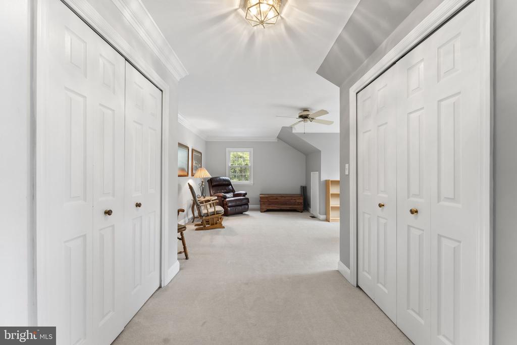 Carpeted hallway with white closets opening into a sitting area with a recliner and rocking chair.