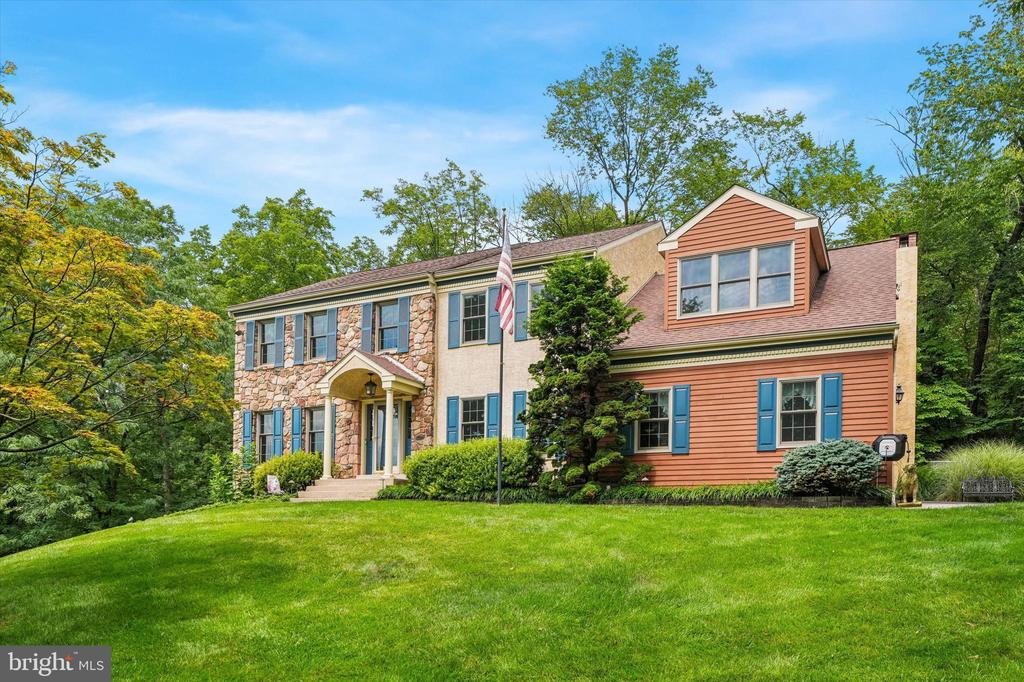 Two-story home with stone and coral siding, blue shutters, and a broad green lawn.