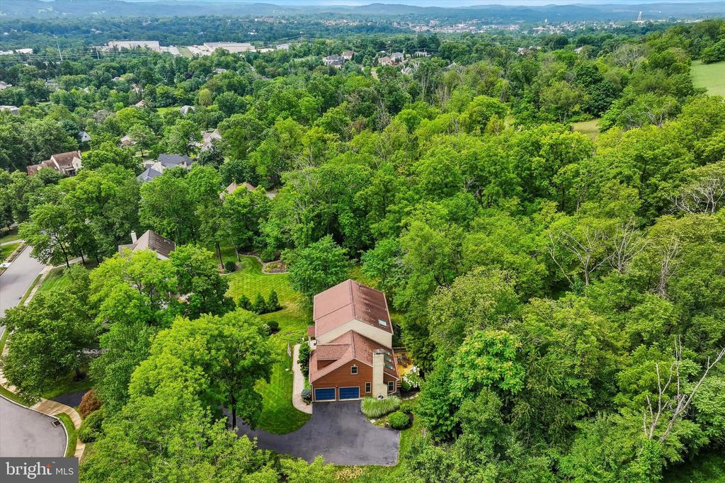 Aerial view of a reddish-roofed home surrounded by mature trees, lawn, and a curved driveway.