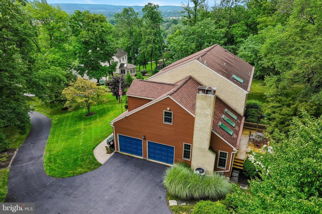 Aerial view of a wooded home with blue garage doors, a curved driveway, and distant mountain ridges.