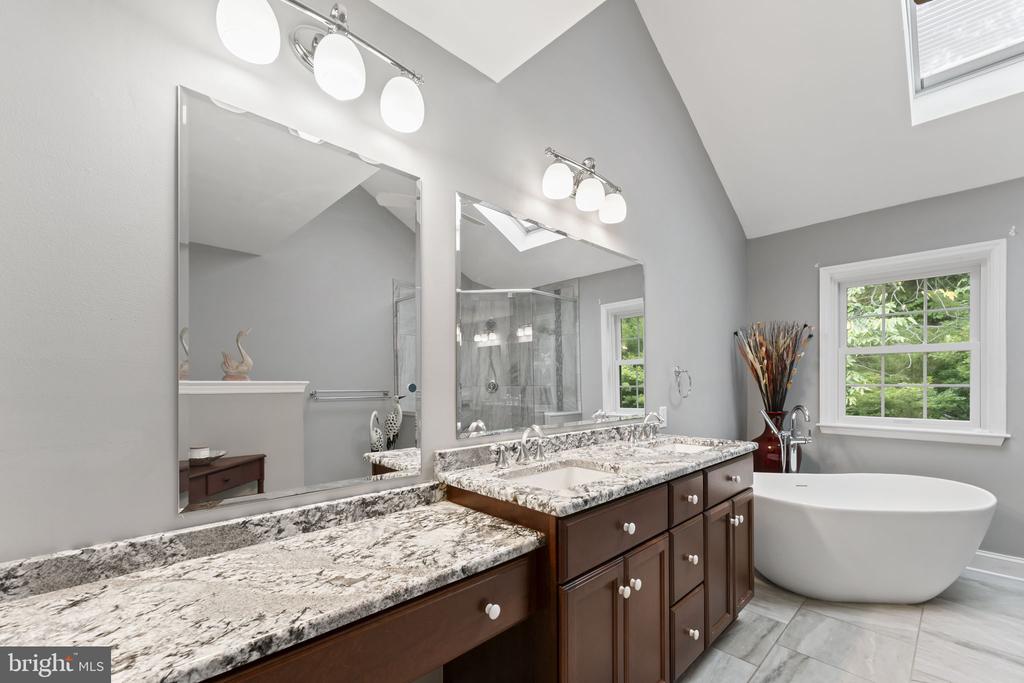 Primary bathroom with a double granite vanity, glass shower, and freestanding soaking tub.
