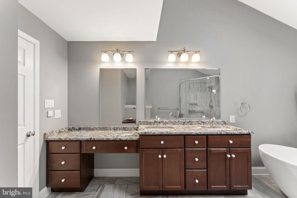 Bathroom with a dark wood double vanity, granite countertop, glass shower, and freestanding tub.