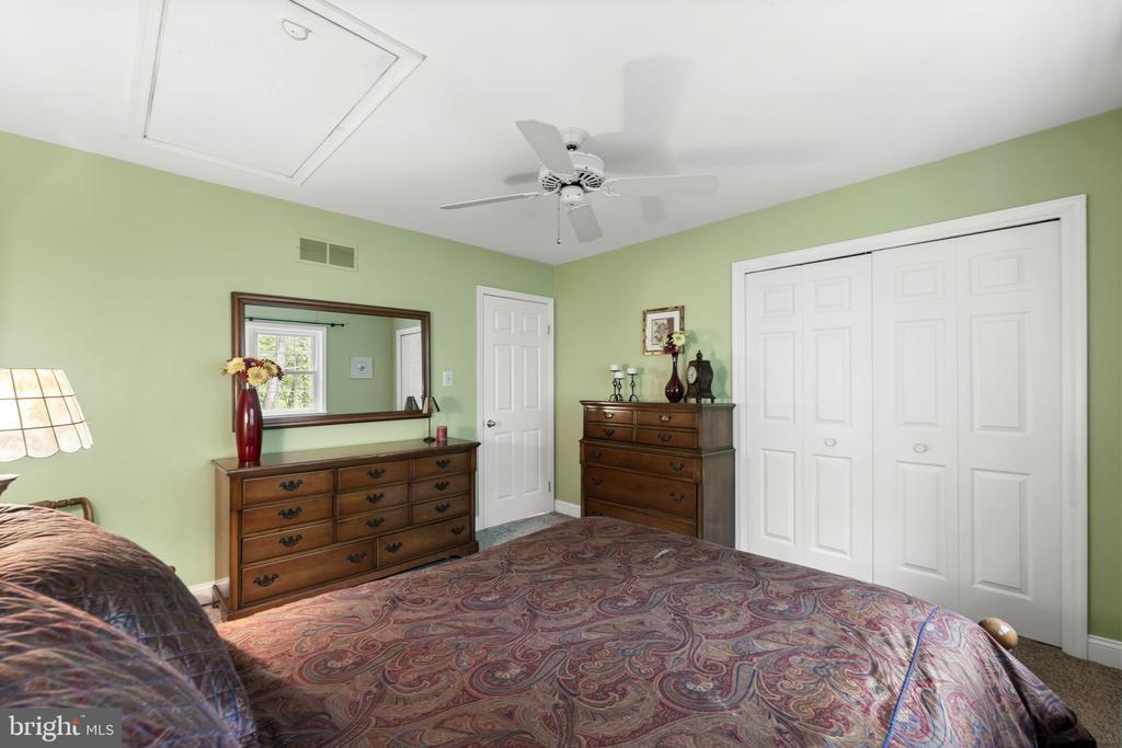 Bedroom with pale green walls, patterned bedspread, wooden dressers, and white closet doors.