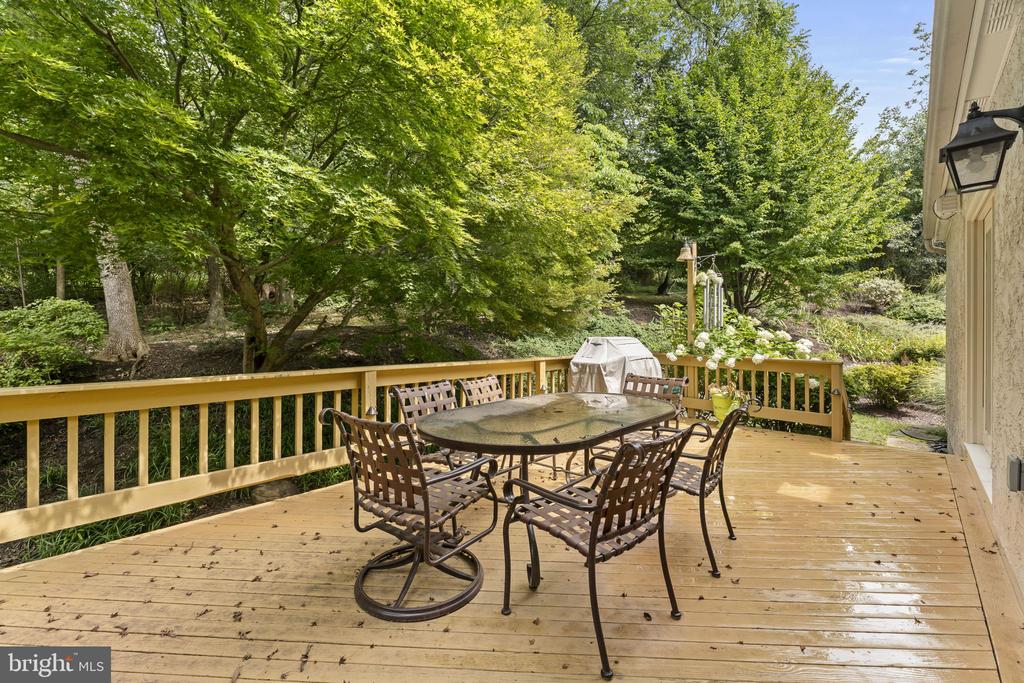 Furnished wooden deck with a glass-top table and chairs overlooking a leafy yard.