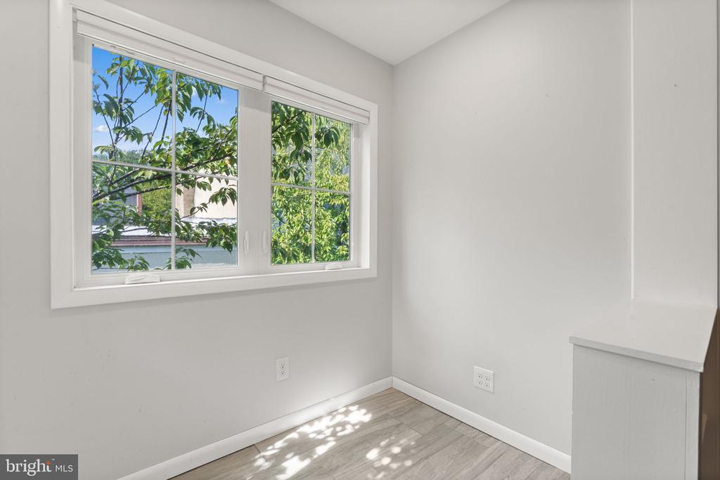 Empty room with gray plank flooring and a large window overlooking leafy trees.