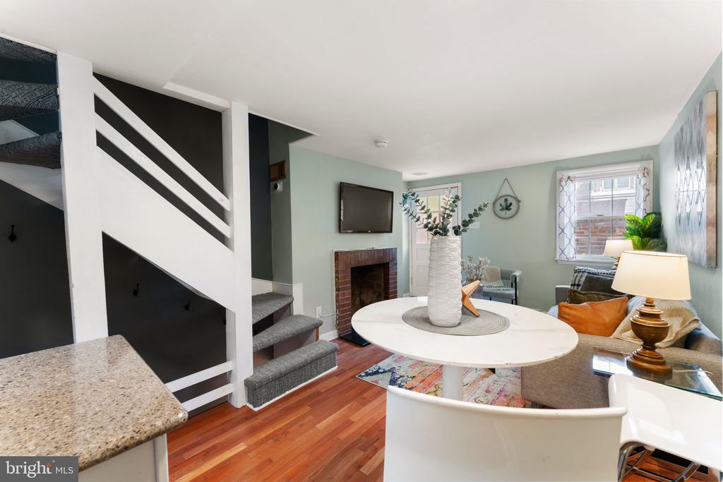 Living and dining area with a brick fireplace, white staircase, and reddish hardwood floors.