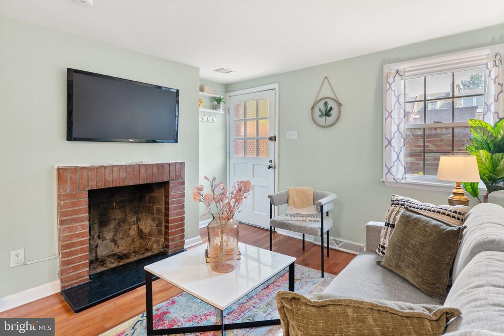 Furnished living room with a brick fireplace, wall-mounted television, hardwood floors, and a large window.
