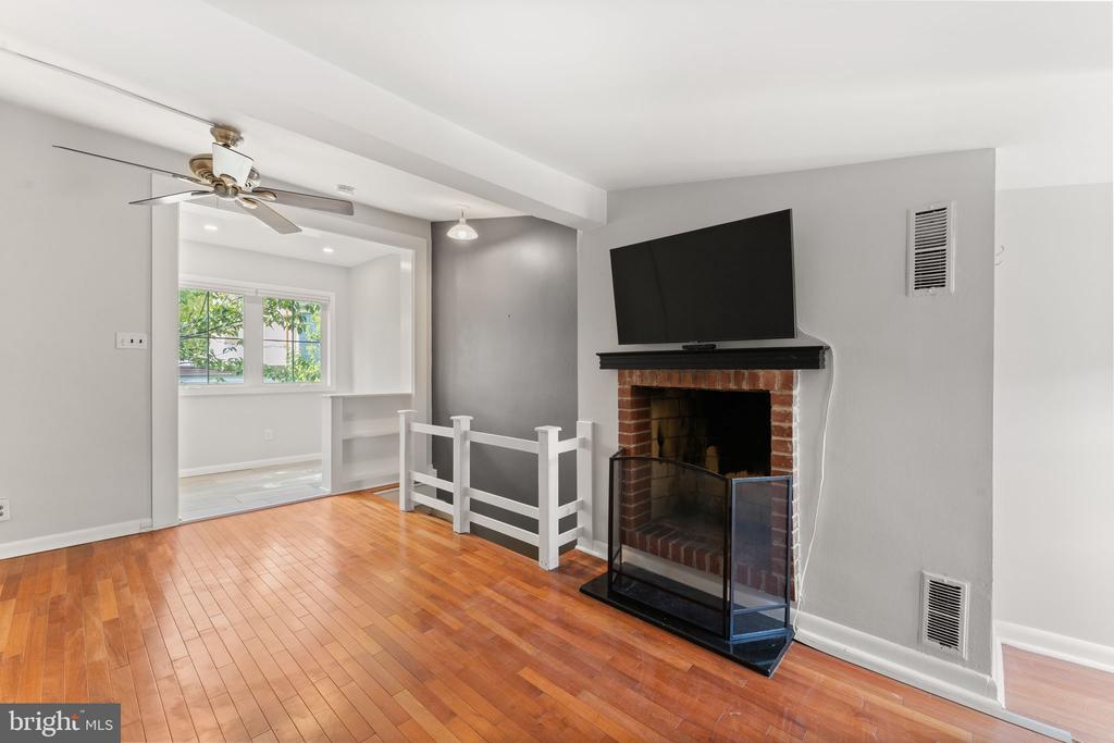 Unfurnished living room with hardwood floors, brick fireplace, mounted television, and a bright adjoining room.