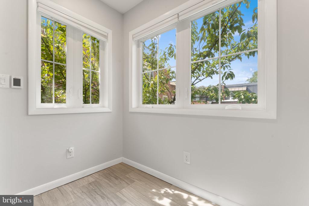 Empty room with light wood-look flooring and two large windows overlooking leafy trees.