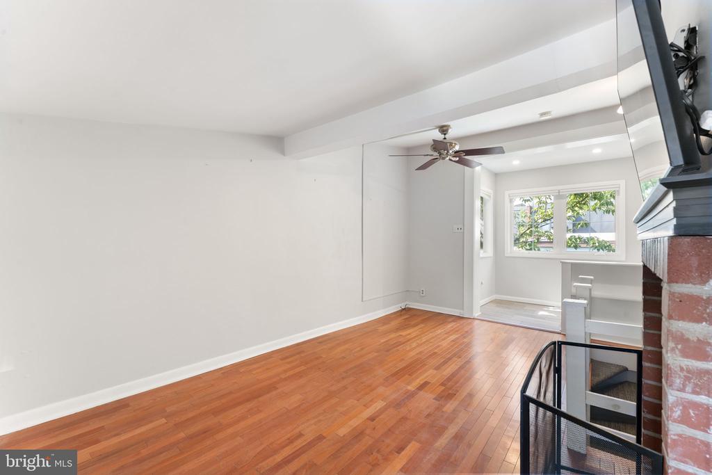 Empty living room with polished hardwood floors, a brick fireplace, and large windows.