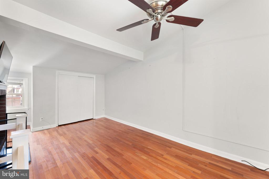 Mostly empty room with hardwood floors, a ceiling fan, and sliding-door closet.