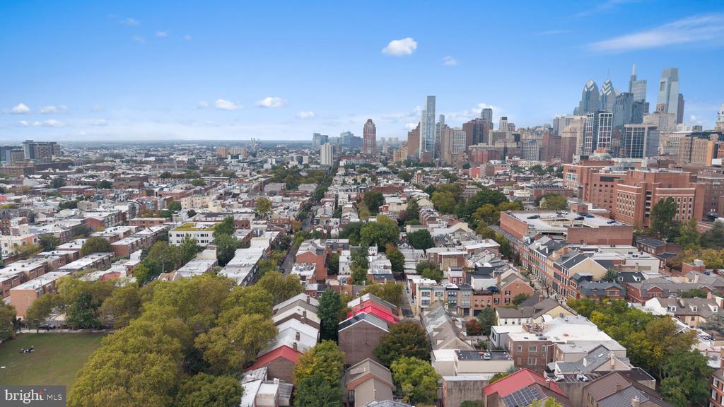 Aerial view of Philadelphia rooftops and downtown skyline, with a tree-lined park in the foreground.