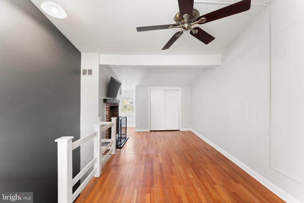 Unfurnished living area with hardwood floors, a dark accent wall, and a brick fireplace with mounted TV.