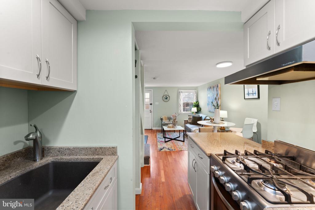 Kitchen opening to a furnished living and dining area, with granite counters and a stainless steel gas range.