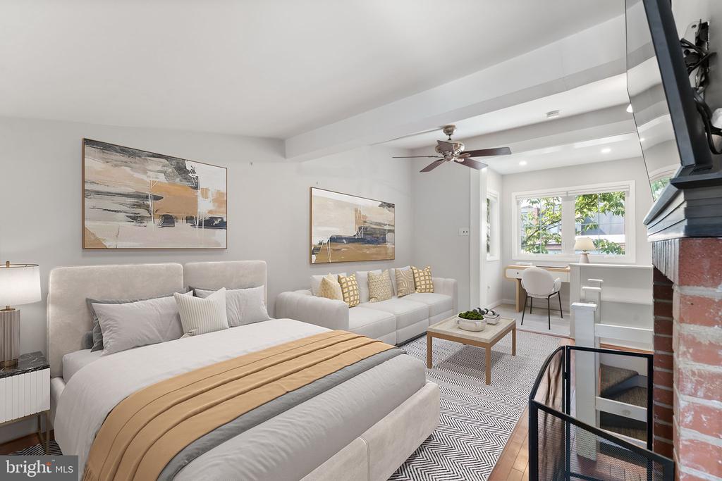 Open-plan bedroom and living area with a large bed, sofa, abstract art, and desk by the windows.