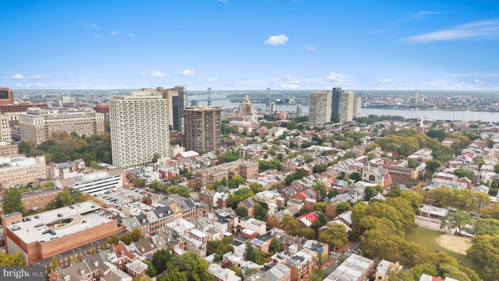 Aerial view of Philadelphia rooftops, with distant high-rises, river and bridges.