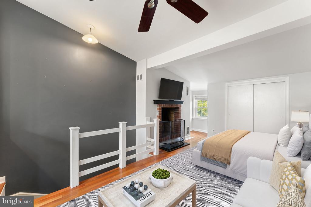 Bedroom with a brick fireplace, television, dark accent wall, and white railing.