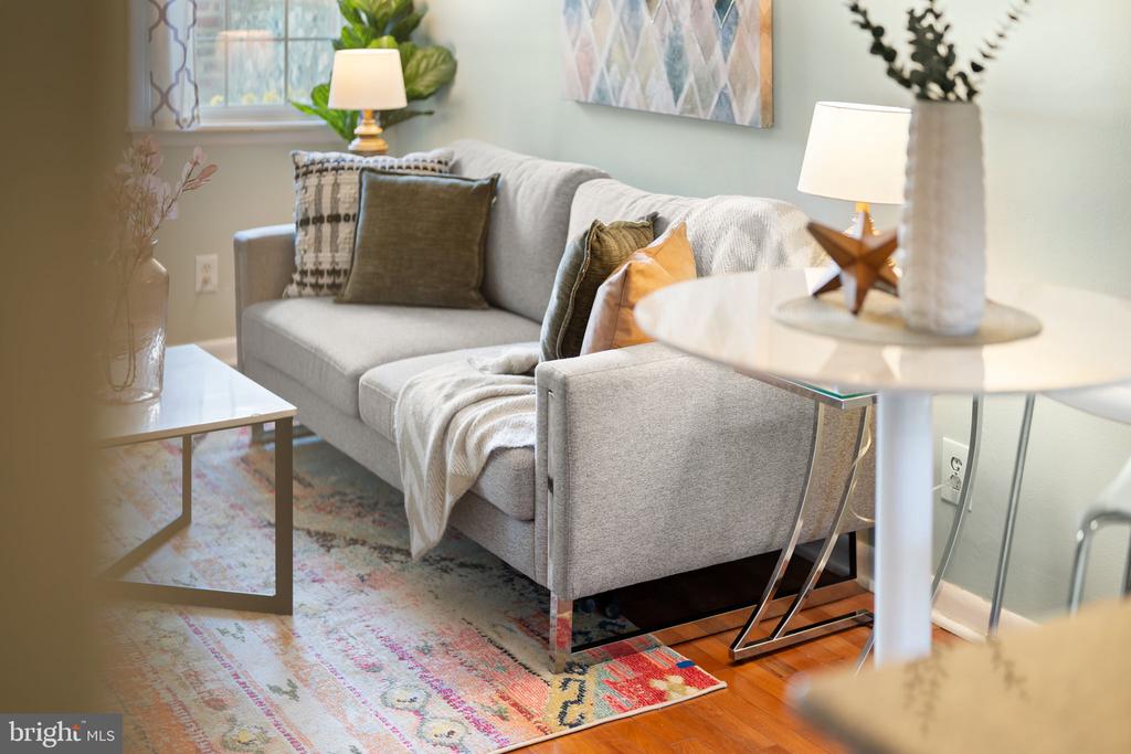 Staged living room with a gray sofa, colorful patterned rug, and hardwood floors.