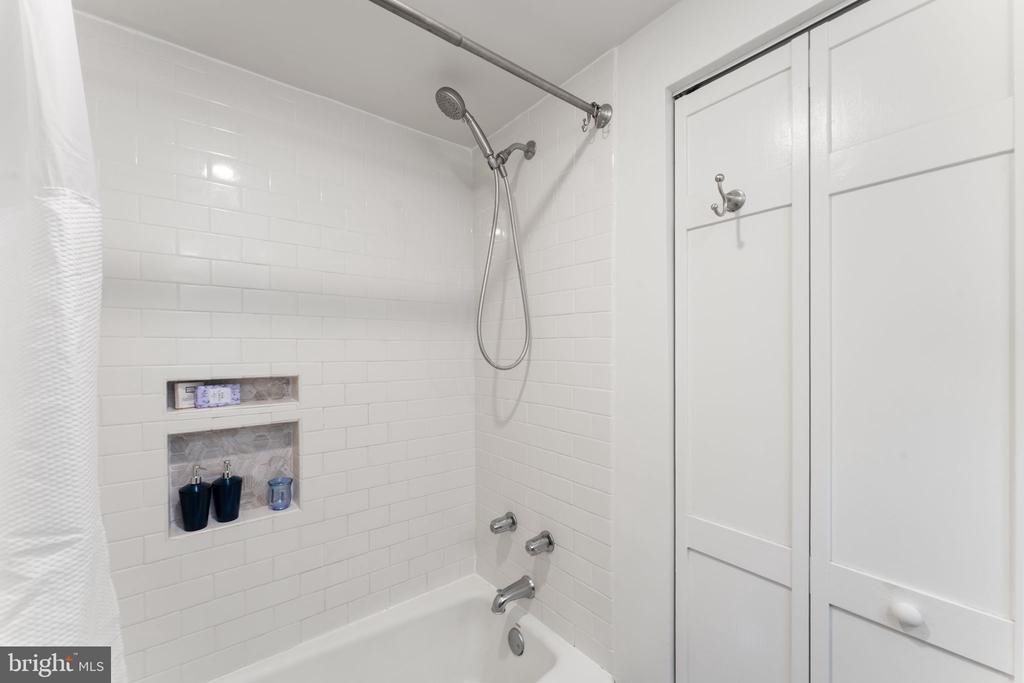 White-tiled bathtub and shower with recessed niches and tall built-in cabinets.