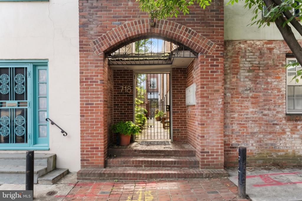 Brick-arched gated entrance at 718 Addison Street, with a small courtyard and potted plants.
