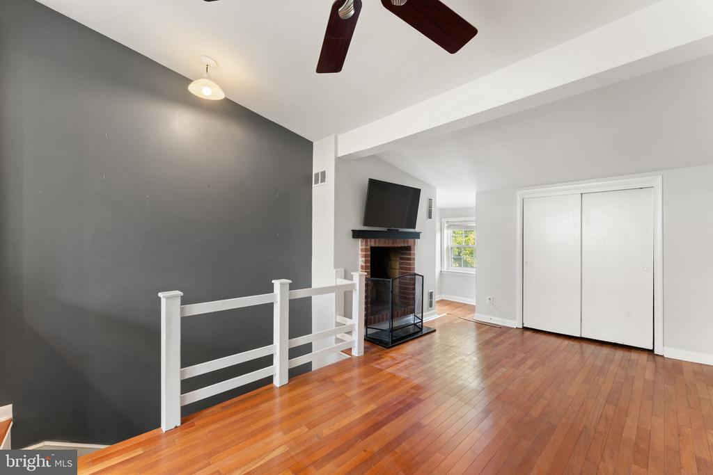 Living area with hardwood floors, a brick fireplace, and a white railing beside an open stairwell.