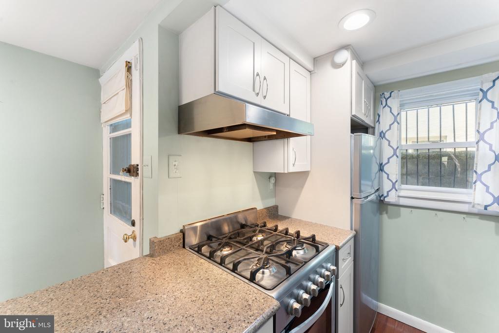Compact kitchen with a stainless steel gas range, speckled counters, and blue-and-white window curtains.