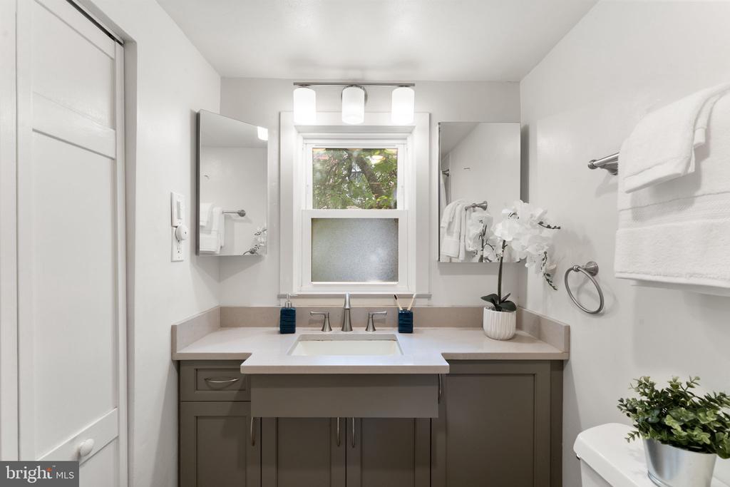 Bathroom vanity with mirrored cabinets, a window, white towels, and a potted orchid.