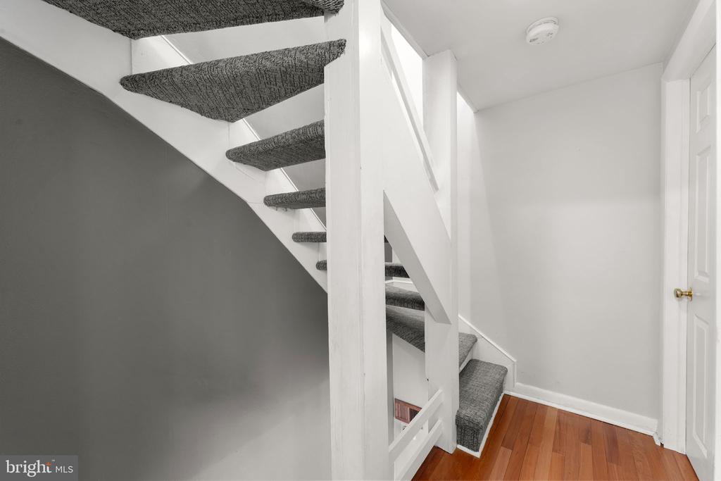 Carpeted staircase with white railings beside a hardwood-floored landing.