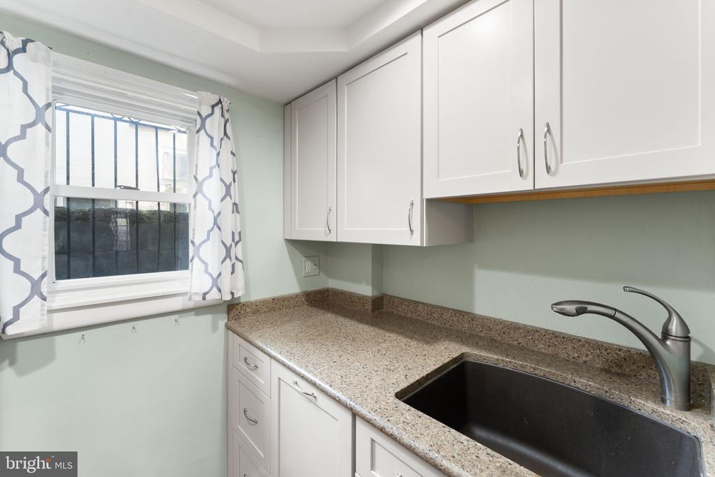 Kitchen with white cabinets, speckled counters, a dark sink, and patterned curtains at the window.