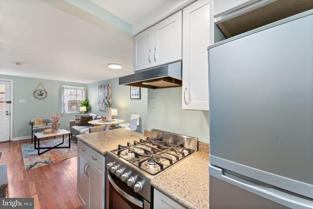 Kitchen with granite counters and stainless steel appliances opening onto a furnished living area.