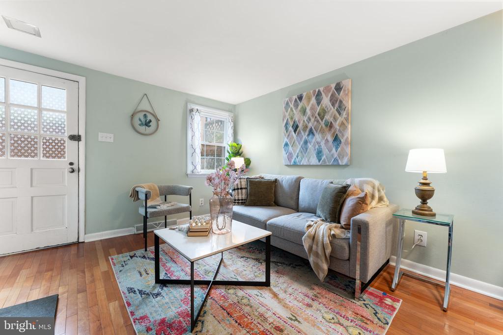 Staged living room with a gray sofa, sage-green walls, and colorful patterned rug.