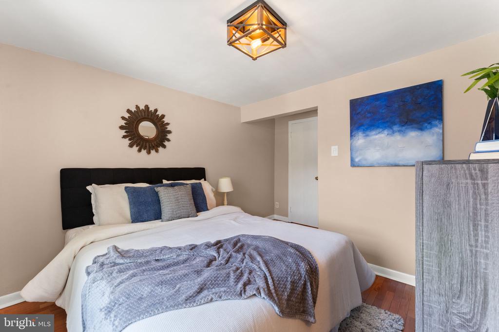 Staged bedroom with a large bed, blue-gray accents, hardwood floors, and abstract blue wall art.