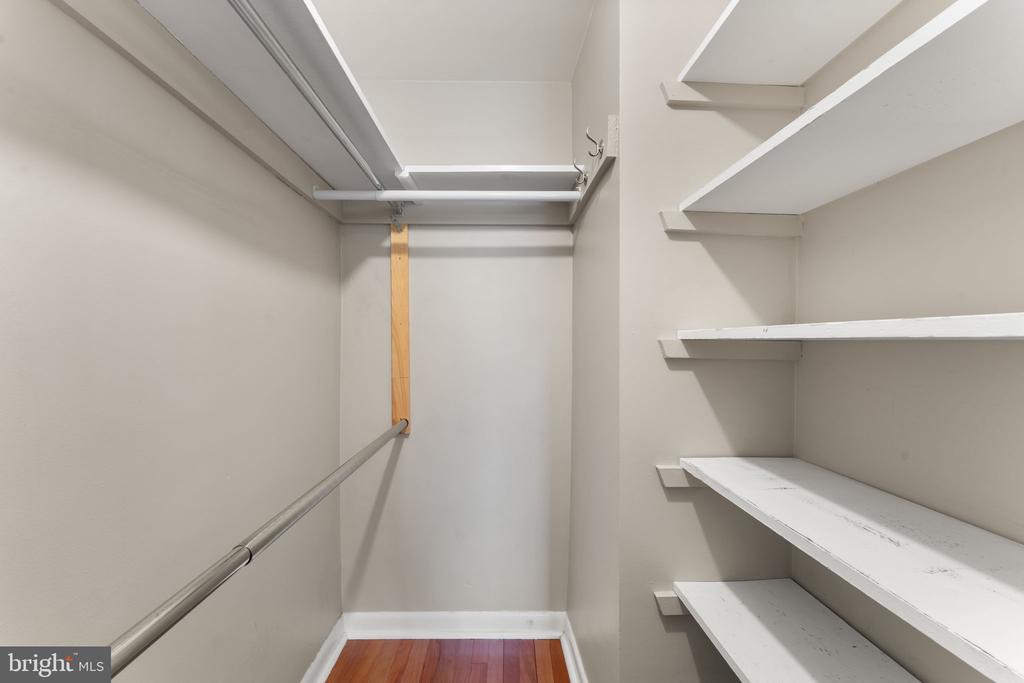 Walk-in closet with built-in shelves, a hanging rod, and reddish wood flooring.