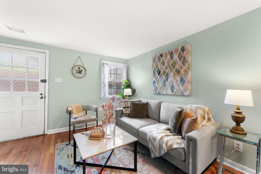 Living room with a gray sofa, sage-green walls, abstract artwork, and hardwood floors.