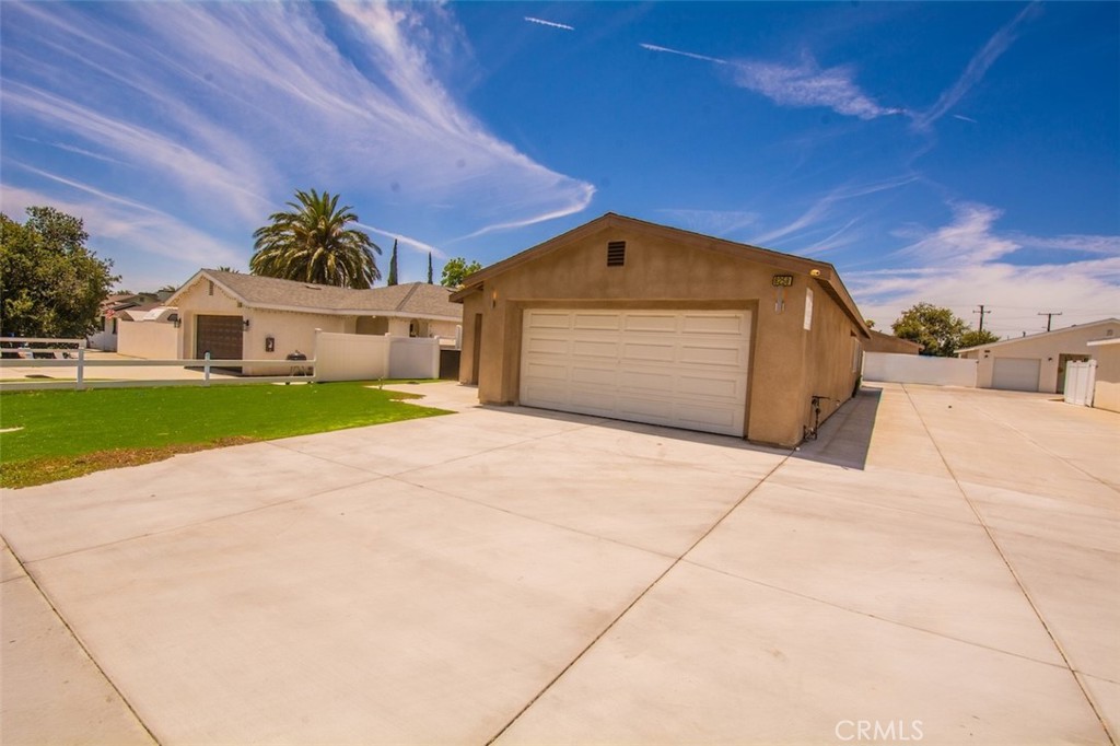 Tan detached garage with a white double door and a broad concrete driveway.