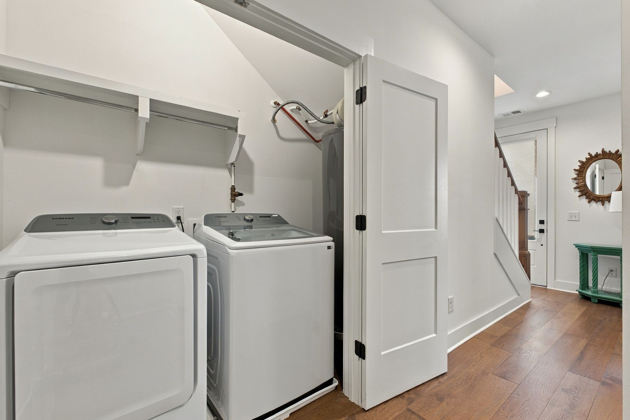 Laundry closet with a washer and Samsung dryer beside a hardwood-floored hallway.
